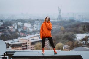 chica con una chaqueta naranja posa en el techo de un edificio en el centro de la ciudad foto