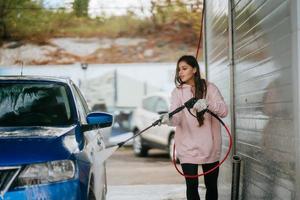 Young woman washing blue car at car wash photo