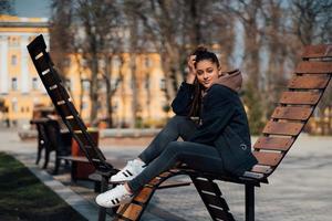 mujer joven sentada en un banco en el parque, sonriendo y mirando a la cámara foto