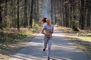 Beautiful young woman running in green park on sunny summer day photo