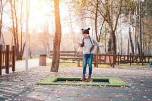 Happy school girl jumping on a small trampoline in the park photo