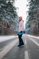 Skateboarder standing on the road in the middle of the forest, surrounded by snow photo
