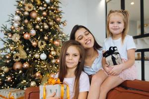 madre y dos hijas pequeñas contra el fondo del árbol de navidad foto