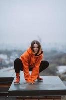 Girl in an orange jacket poses on the roof of a building in the city center photo