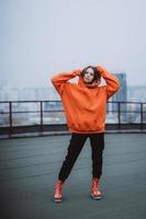 chica con una chaqueta naranja posa en el techo de un edificio en el centro de la ciudad foto