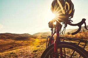 Close up bicycle stand in nature with sunflare peaks through helmet. Cinematic cycle wallpaper. Travel transport red bike photo