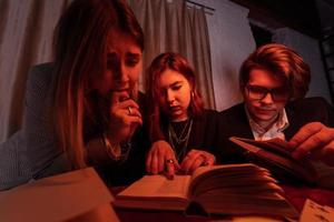 Two women and a guy are reading a mysterious books, close view photo