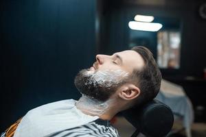 hombre con espuma de afeitar en la cara en una barbería foto