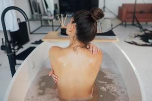 Pretty young woman taking bath at home back view photo