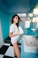 Portrait of young woman using hairdryer in bathroom photo