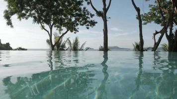 infinite swimming pool with background of natural sea and mountain view with some tree. vacation summer destination video