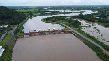 vista aérea del agua liberada del canal de drenaje de la presa de hormigón como desbordamiento en la temporada de lluvias. vista superior de los flujos de agua turbia del bosque marrón desde una presa en el norte rural de tailandia. video