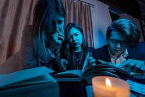 Two women and a guy are reading a mysterious books, close view photo