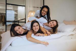 Positive young girls women friends indoors on bed at the hen party at home. photo