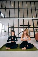 Two young women meditating in lotus pose with hands in namaste. photo