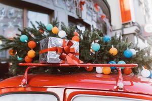 Red retro car with a Christmas tree fir tied to the roof. photo