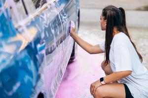 Brunette with two pigtails with a sponge washes the side of the car photo