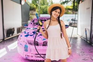 Young woman hose stands in front of a car covered in pink foam photo