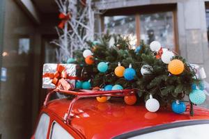 coche retro rojo con un abeto de árbol de navidad atado al techo. foto