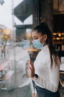 Young woman in face mask standing in front of windows in cafe. photo