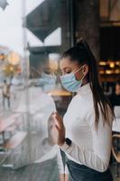 mujer joven con mascarilla parada frente a las ventanas en el café. foto