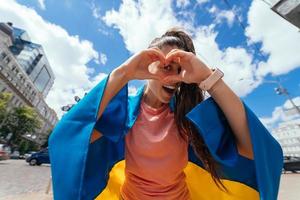 Young woman with Ukrainian flag shows heart with hands photo