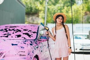 Woman with hose stands by car covered in pink foam photo