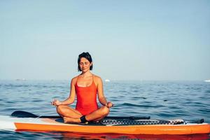 Young woman doing yoga on sup board with paddle photo