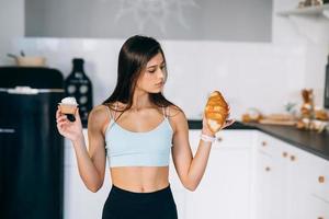 A young woman holds a croissant and a cake in her hands. photo