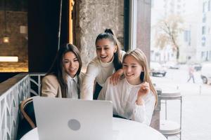 A group of women friends in a cafe are looking at a laptop photo
