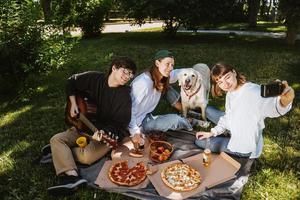 Company of beautiful young people and dog having an outdoor lunch. photo