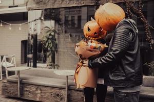 The guy gives his girlfriend a bouquet, both with a pumpkin head photo