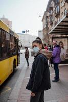 mujer joven con mascarilla quirúrgica al aire libre en la parada de autobús en la calle foto