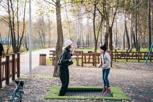 Mom and her daughter jumping together on trampoline in autumn park photo