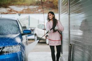 Young woman washing blue car at car wash photo