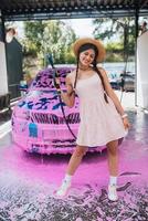 Young woman hose stands in front of a car covered in pink foam photo