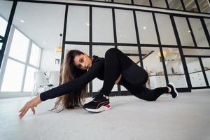 Young female wearing black sports suit exercising yoga pose indoors. photo