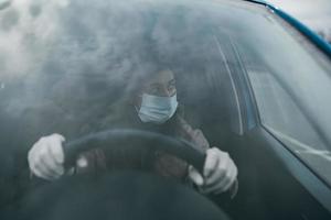 mujer joven con una máscara y guantes conduciendo un automóvil. foto