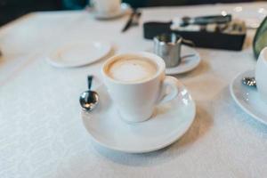 Small white cup of cappuccino stands on the table photo