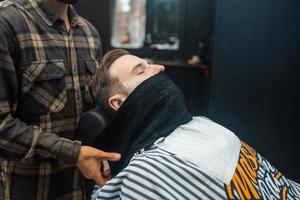 Barber preparing man face for shaving with hot towel in barber shop photo