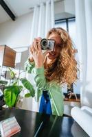 Cheerful young woman making photo on camera at home