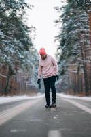 Skateboarder standing on the road in the middle of the forest, surrounded by snow photo