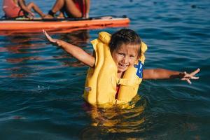 niña pequeña en un chaleco salvavidas bañándose en el mar. foto