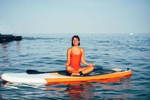 Young woman doing yoga on sup board with paddle photo