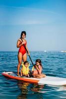 Mother with two daughters stand up on a paddle board photo