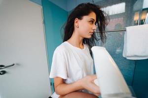 Portrait of young woman using hairdryer in bathroom photo