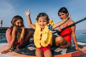 Mother with two daughters stand up on a paddle board photo