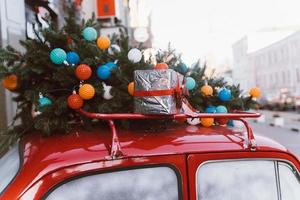 Red retro car with a Christmas tree fir tied to the roof. photo