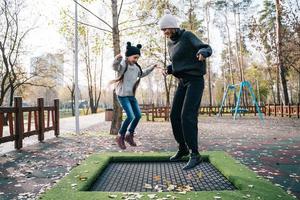 mamá y su hija saltando juntas en trampolín en el parque de otoño foto