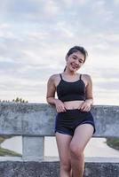 mujer asiática relajándose en un puente después de trotar al atardecer. foto